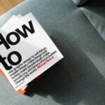 A collection of design books on a couch, showcasing 'How to' by Michael Bierut